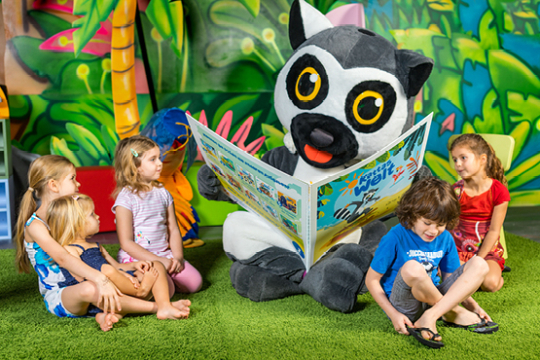 F&uuml;nf Kinder sitzen um Katta herum, der ihnen vorliest